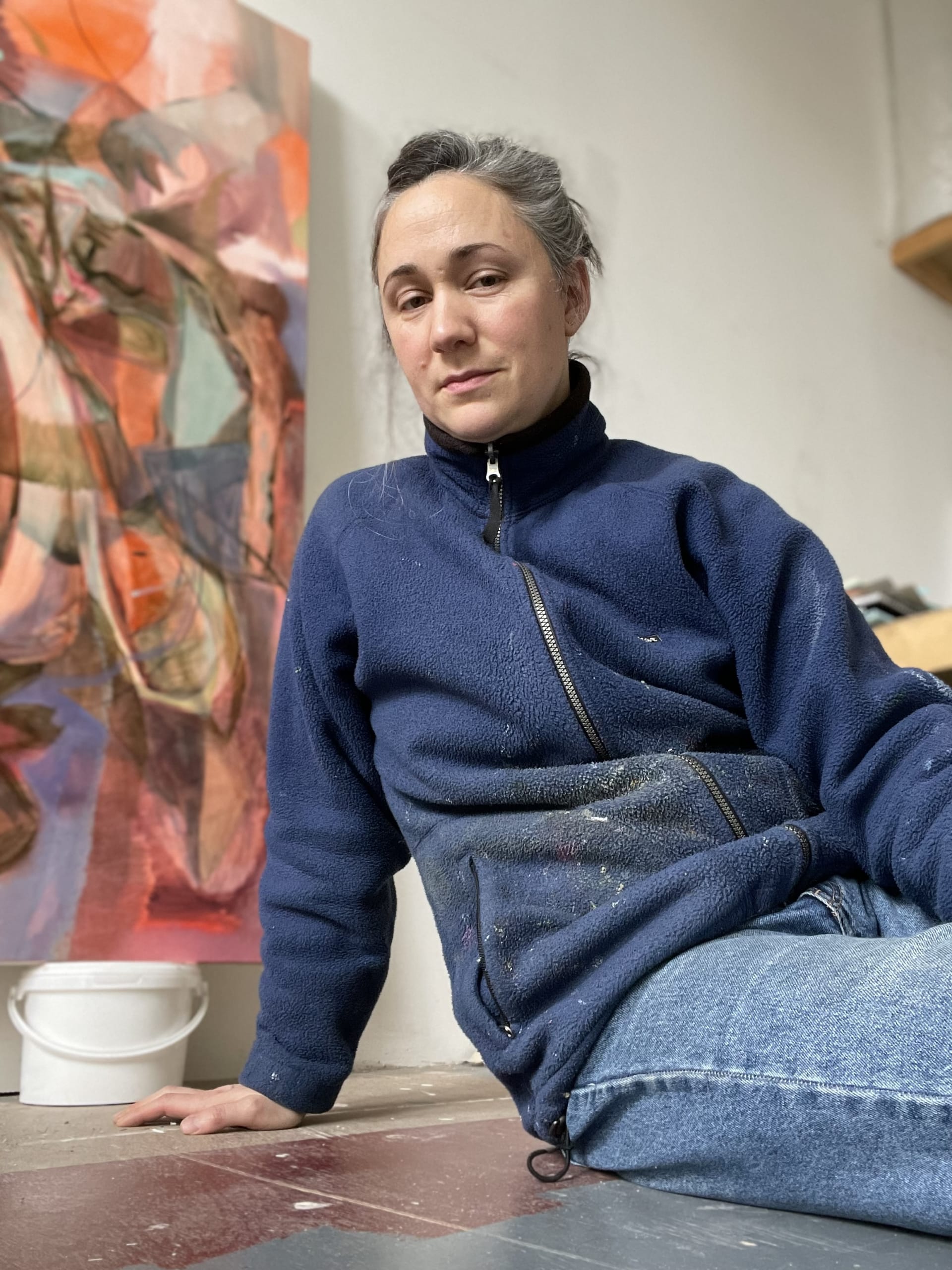 Portrait of artist Amy Winstanley sitting in her studio in front of a painting