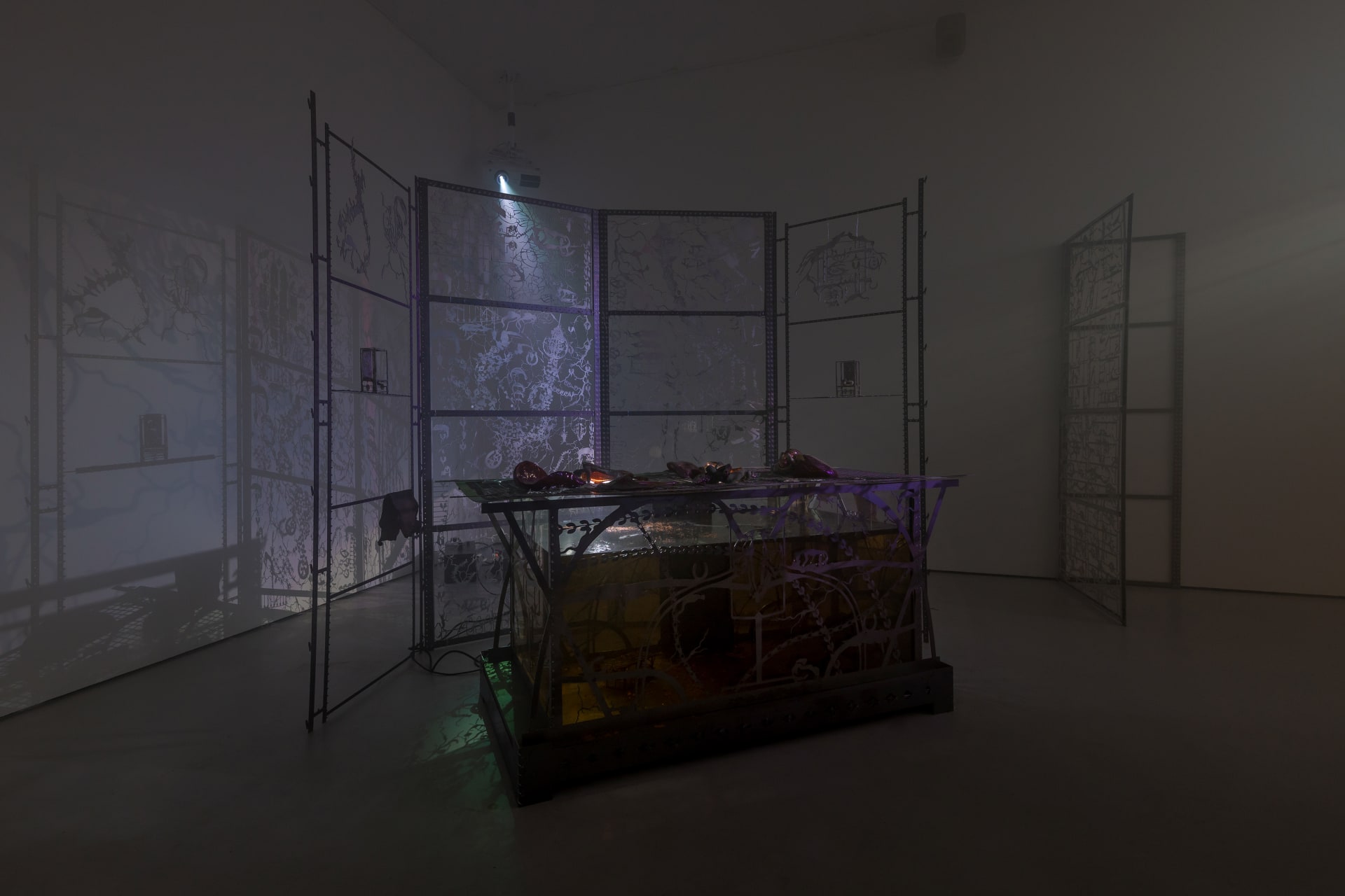 An installation by Hazel Brill including a water tanks filled with a dark liquid laser cut steel dividers, mouth-blown glass objects, projections and lights