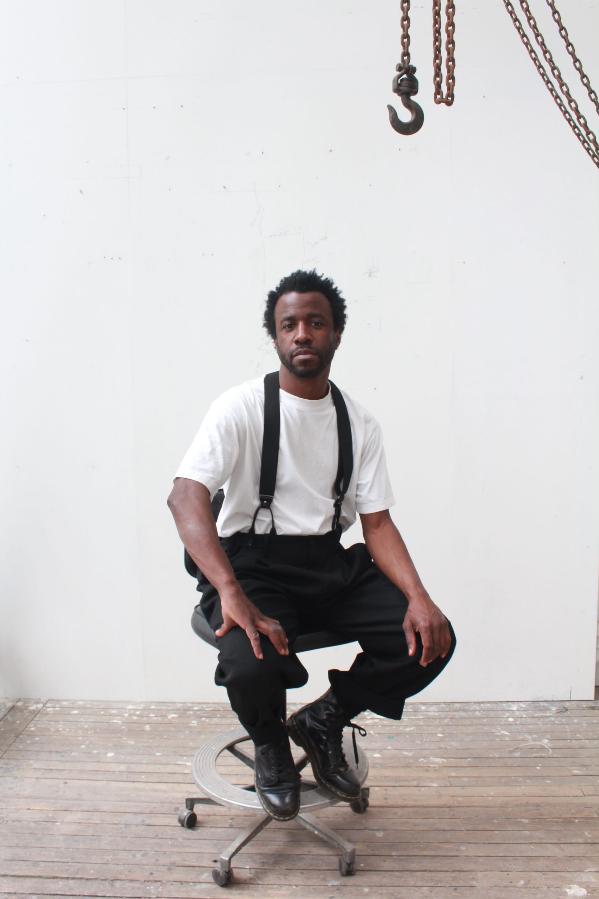 Portraits of artist Simeon Barclay wearing a black suit with white shirt in a minimal semi-industrial setting 