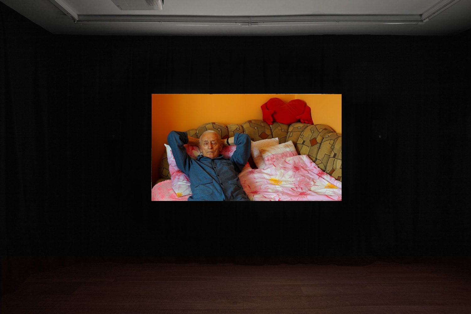 An installation image of Agnieszka Szczotka's film in Workplace's gallery in Margaret Street - an elderly man in pyjamas sleeps on a bed or sofa