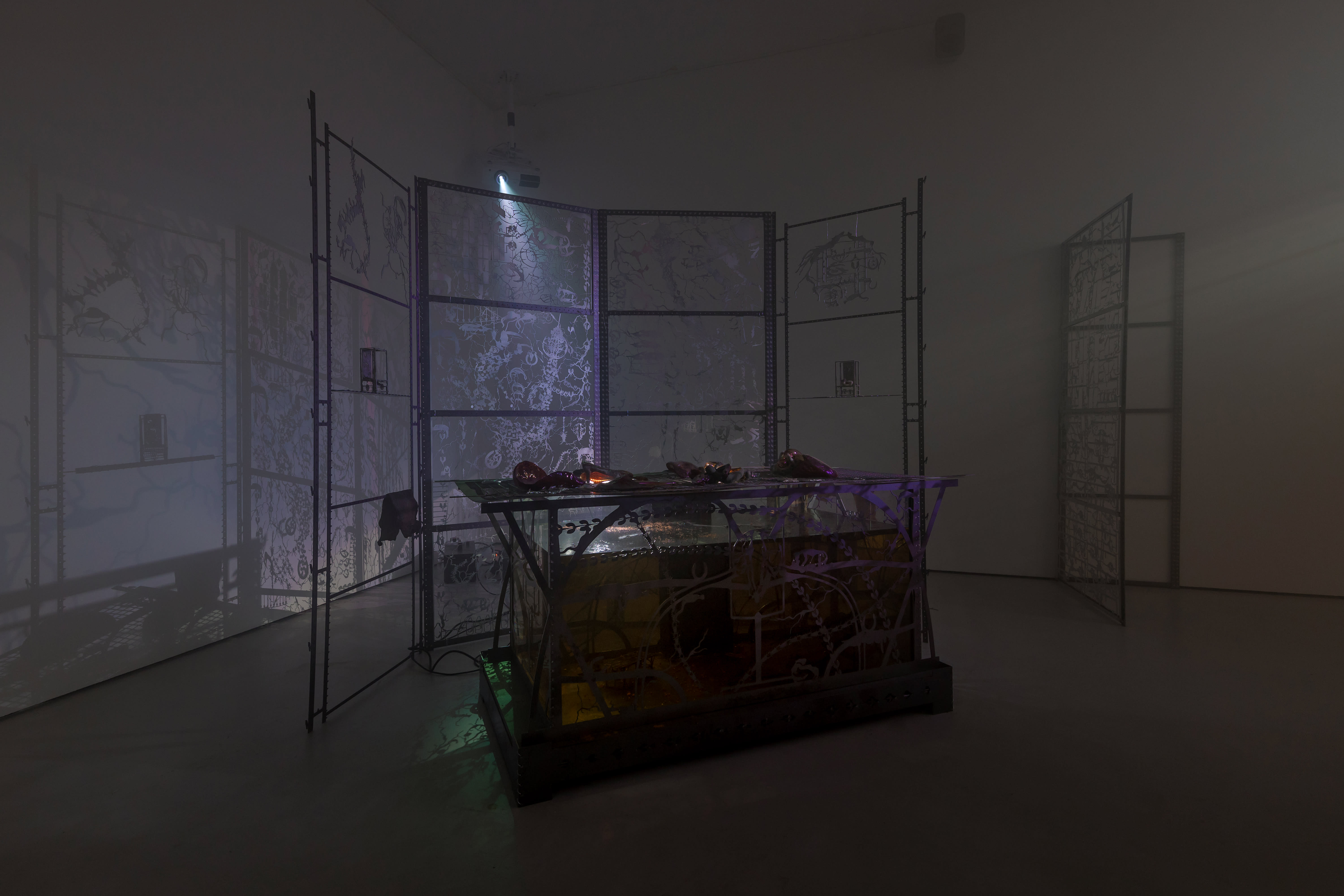 An installation by Hazel Brill including a water tanks filled with a dark liquid laser cut steel dividers, mouth-blown glass objects, projections and lights
