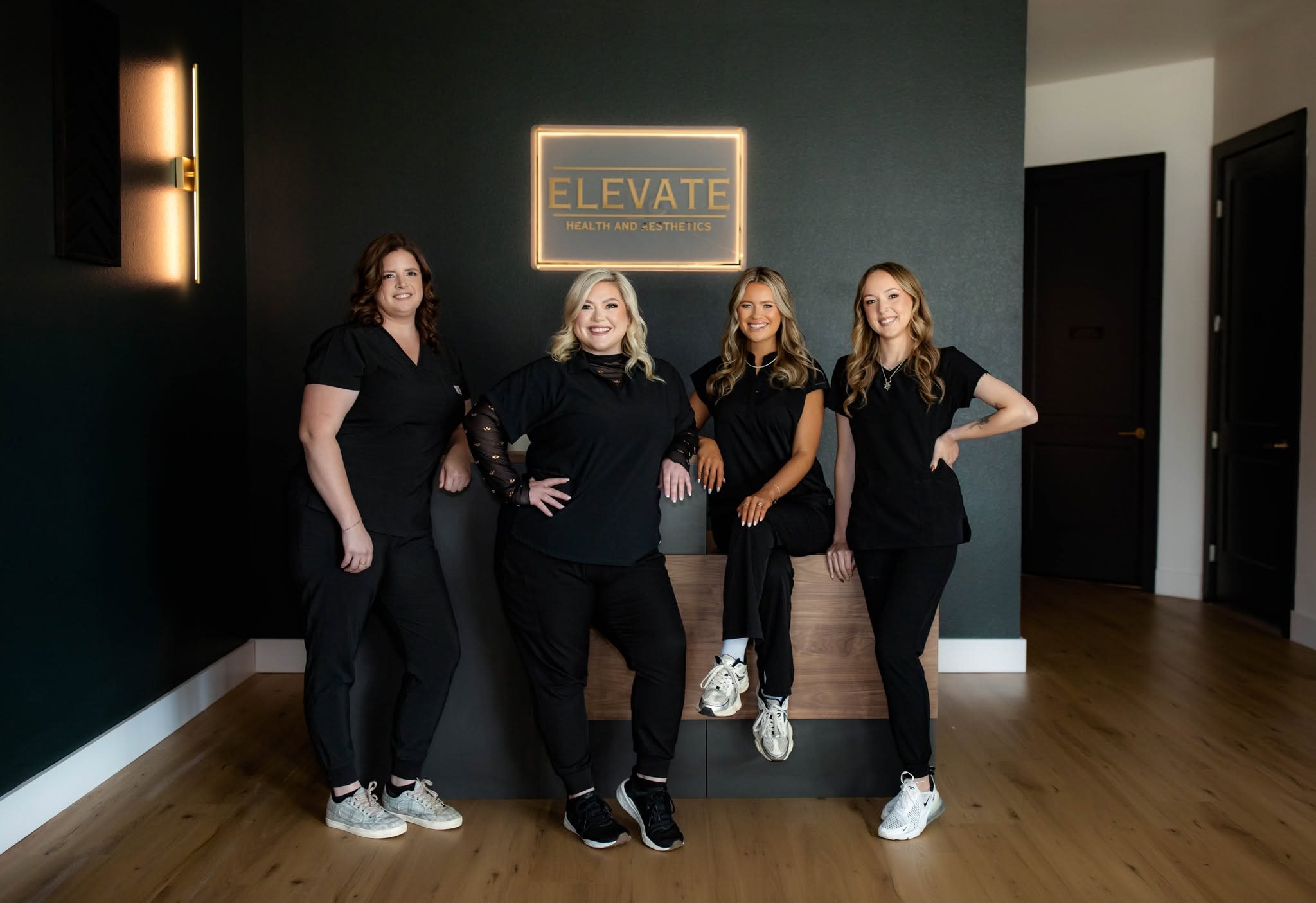 The Elevate Health & Aesthetics team at the reception desk beneath the lit clinic sign