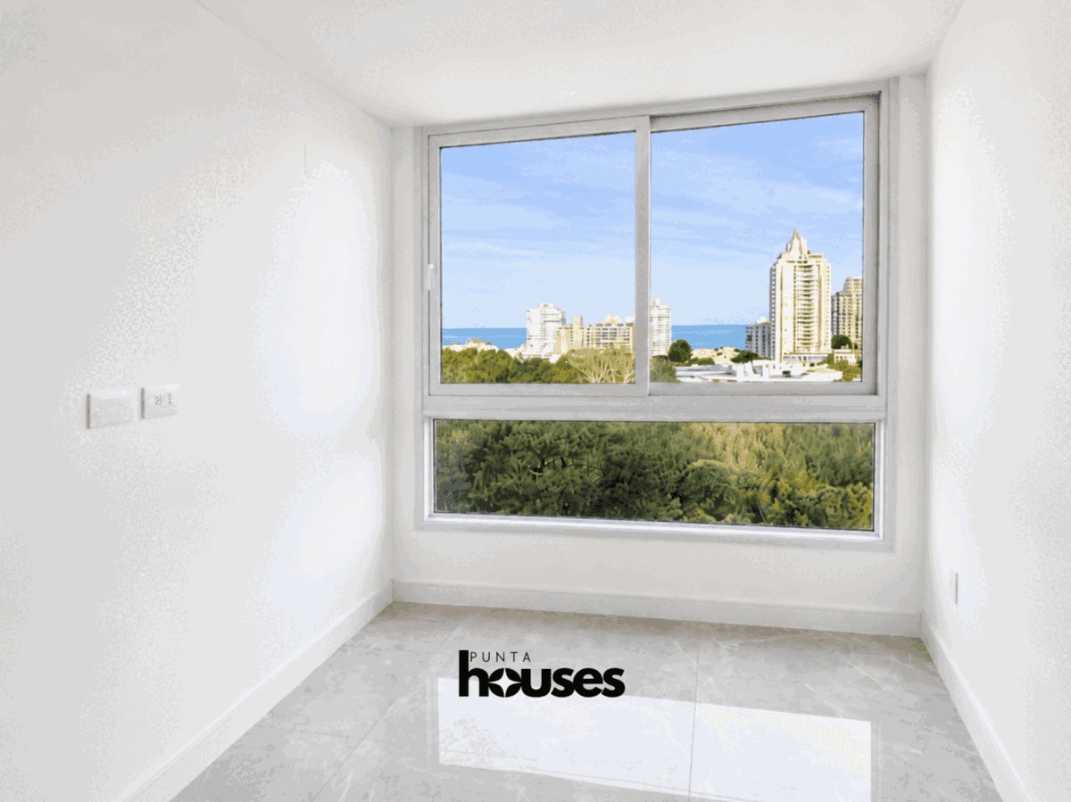 Bright bedroom featuring a large panoramic window overlooking the surrounding forest, city skyline and sea.