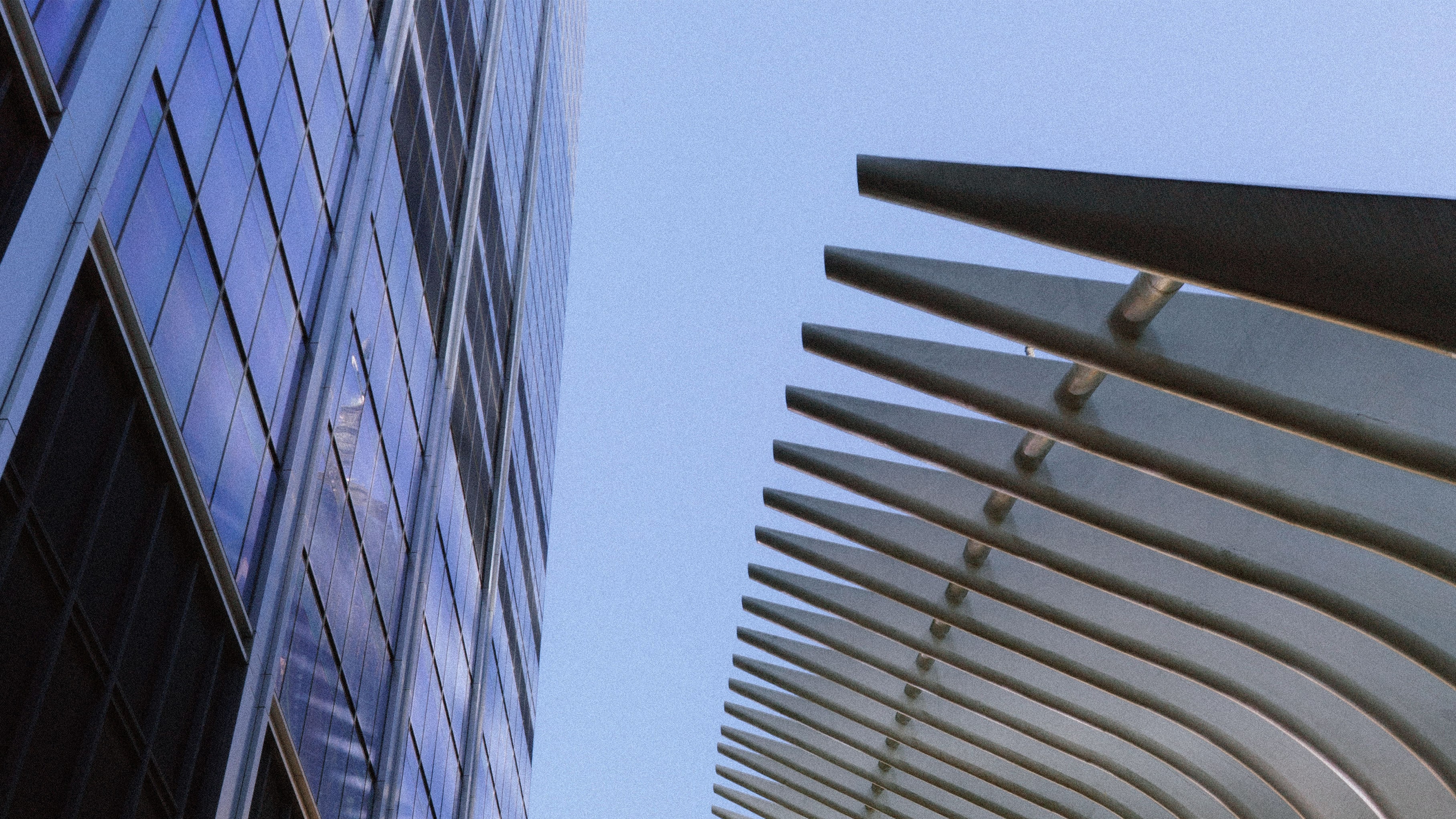 Low-angle view of a blue glass skyscraper on the left and the white, ribbed structure of the Oculus on the right, against a clear blue sky.