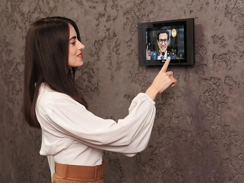 אישה עונה לשיחת וידאו ממוניטור אינטרקום IP חכם המותקן על קיר בתוך הבית
