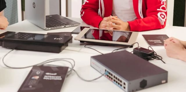 פאנל כניסה ומסך של BAS-IP מחוברים למתג PoE על שולחן ישיבות, בהדגמה של מערכת אינטרקום IP