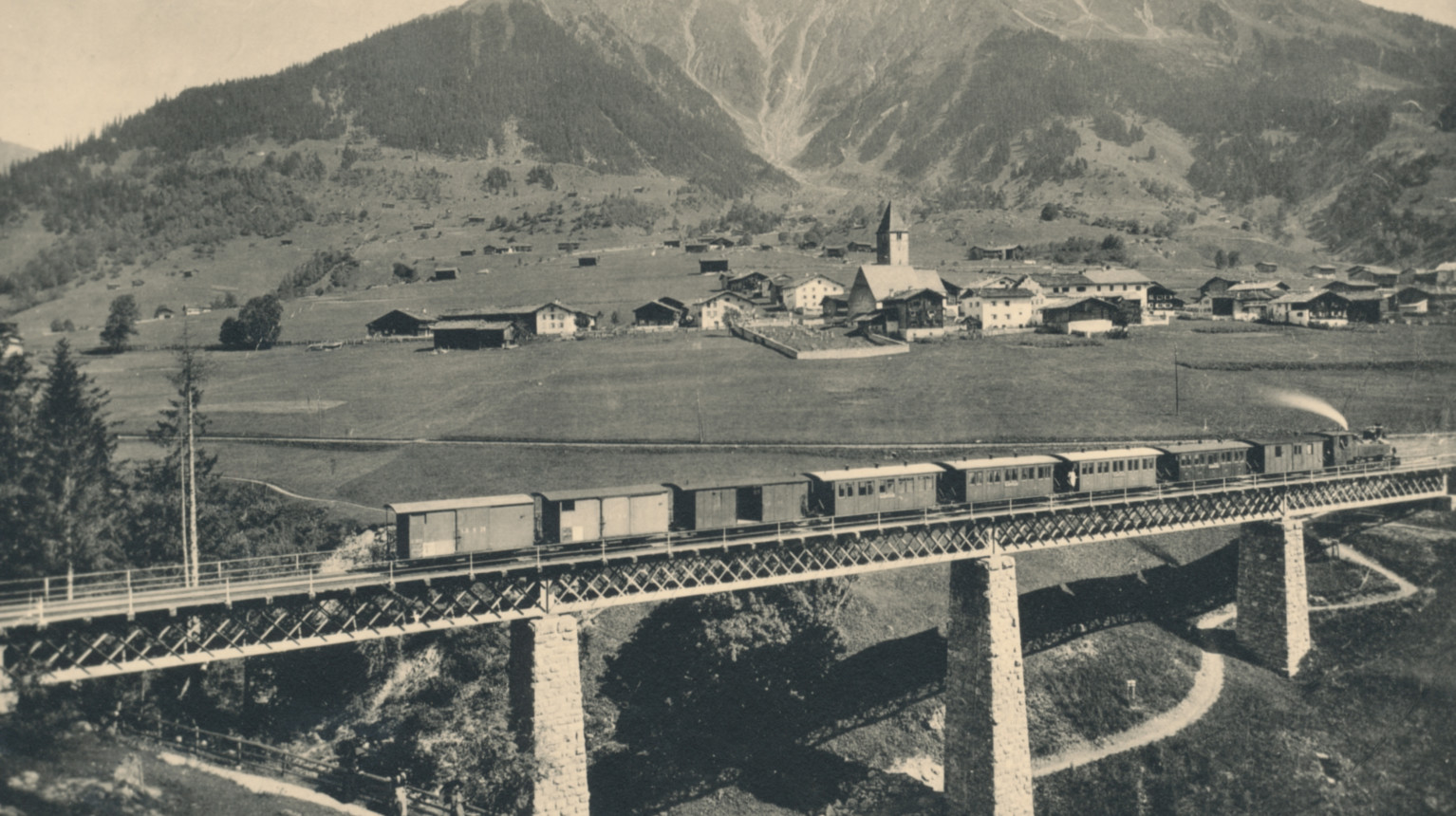 Dampfzug um 1900 auf der alten Eisenbahnbrücke, die heute im Winter von Skifahrer:innen benutzt wird (Archiv Verein Klosters Tourismus / Fotostiftung Graubünden / DDK, M. Jörger).