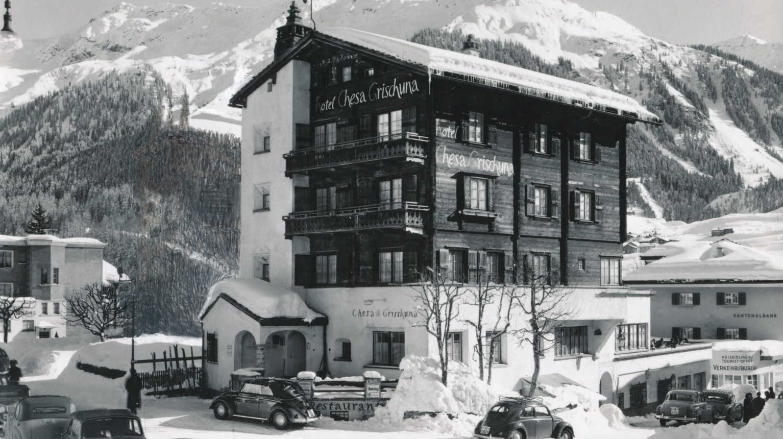 Die Chesa Grischuna mit der Kantonalbank und dem Verkehrsbureau / Reisebureau / Tourist-Office – heute Tourist-Info der Destination Davos Klosters – am rechten Bildrand, undatierte Aufnahme (Archiv Verein Klosters Tourismus / Fotostiftung Graubünden).