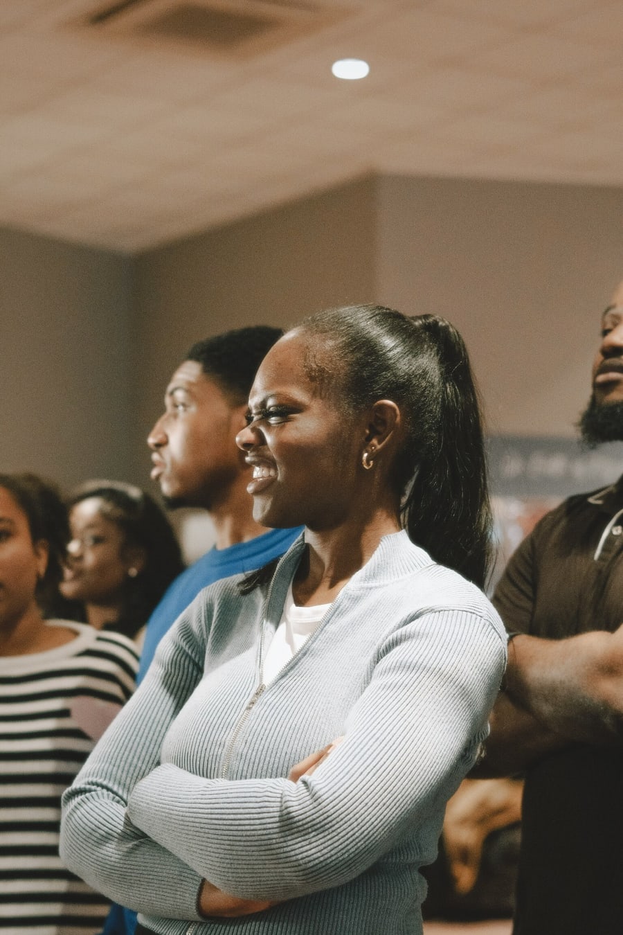 A woman in a cream cardigan stands attentively among the congregation.
