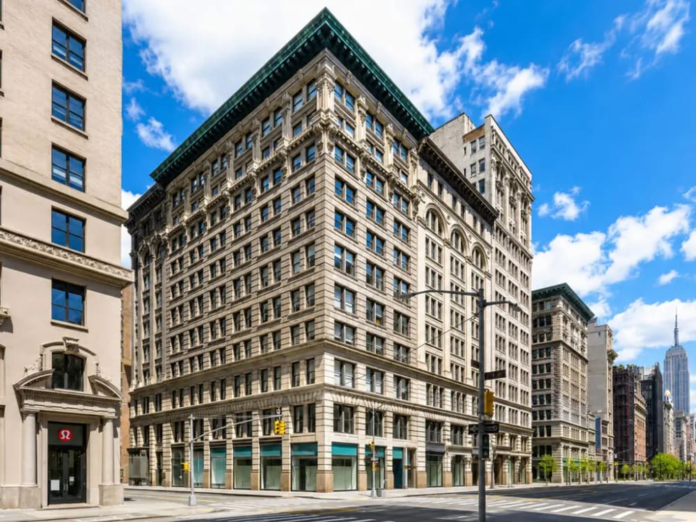 Exterior of a cast-iron loft building on Fifth Avenue in Flatiron with a real estate for-sale rider posted in the ground-floor window