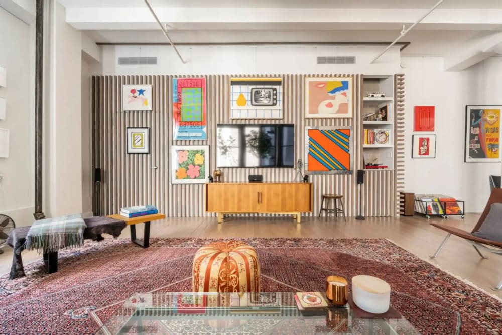 Bright loft living room in a converted Flatiron building with an exposed painted ceiling beam, a gallery wall of art, and wide-plank hardwood floors