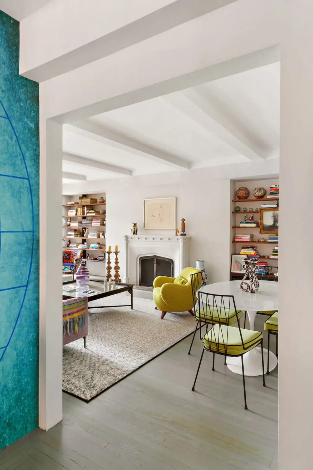 Prewar Manhattan apartment living room with a beamed ceiling, fireplace, built-in bookshelves and a yellow armchair
