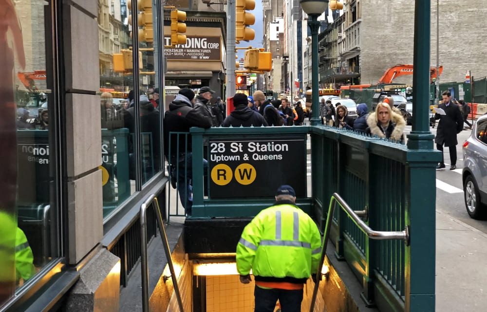 Commuters walking toward a NoMad subway entrance on a weekday morning, Beaux-Arts loft buildings behind them