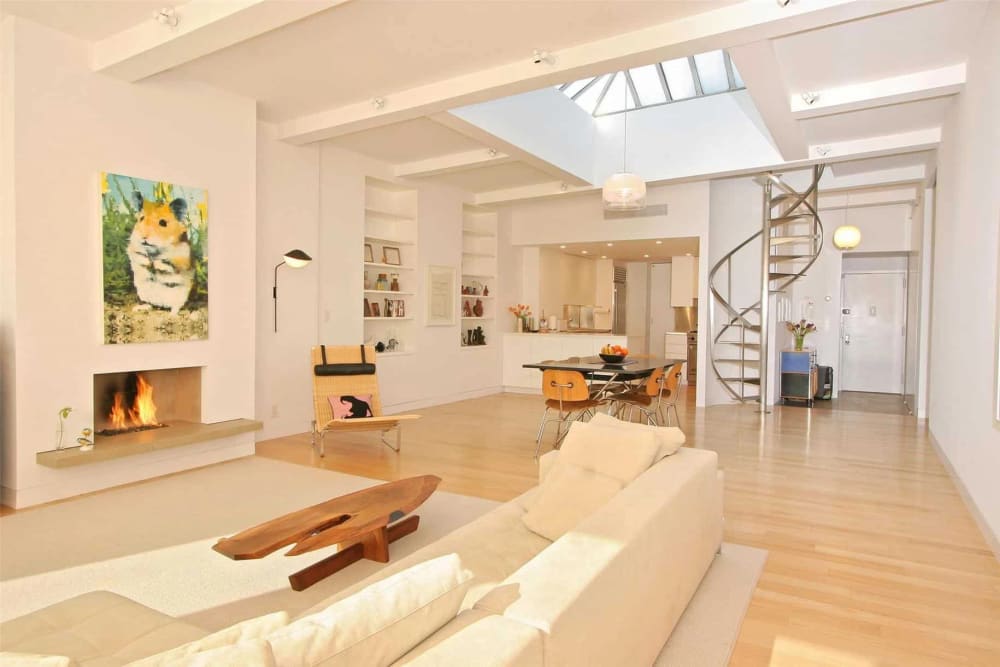 Bright, open-plan loft interior with exposed ceiling beams, a skylight, spiral staircase, and wide-plank hardwood floors