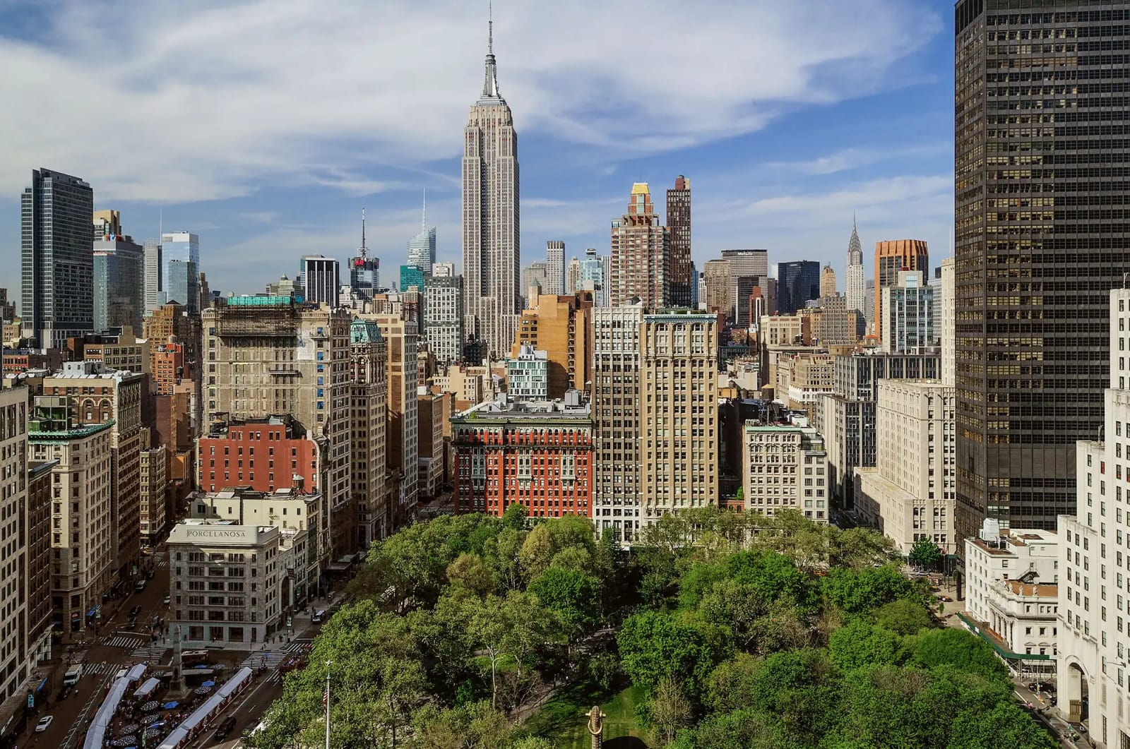 Daytime aerial view over Madison Square Park toward Midtown Manhattan, with the Empire State Building rising above the NoMad and Flatiron skyline