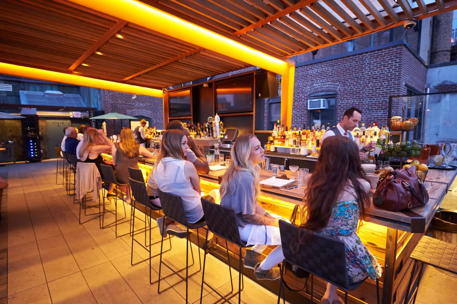 Crowd of people drinking cocktails on a New York City rooftop bar at sunset with the skyline in the background