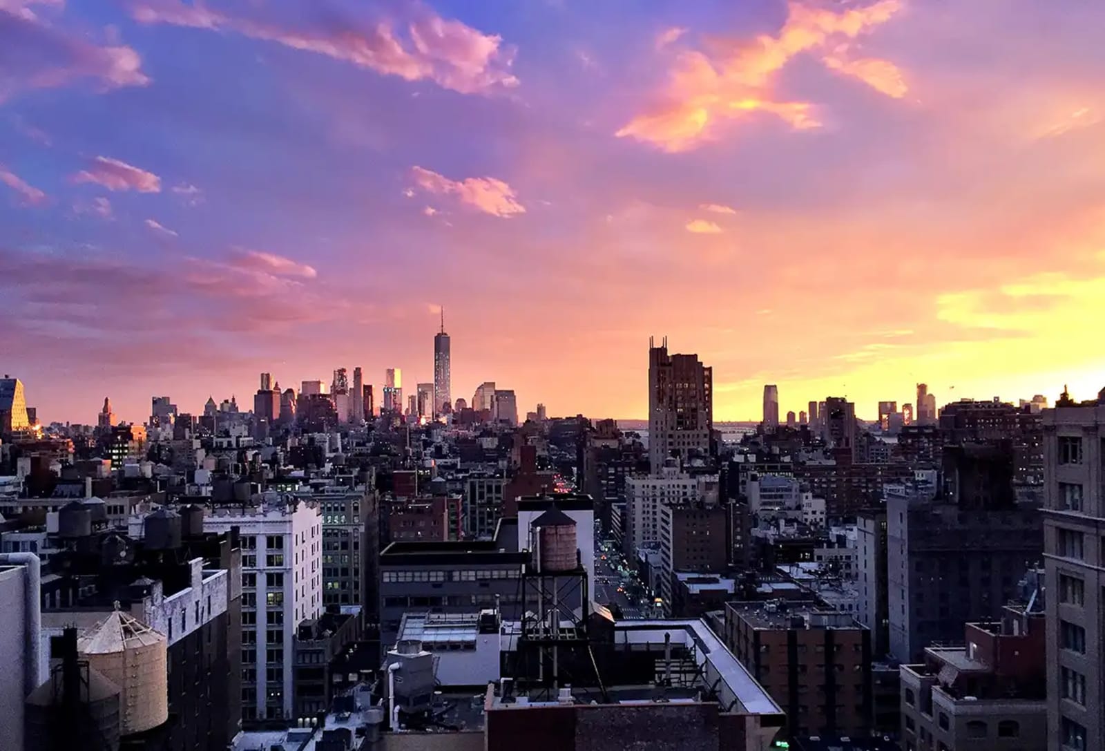 Manhattan skyline at sunset with rooftop water towers and One World Trade Center on the horizon
