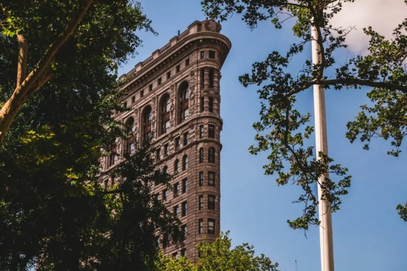Exterior of a cast-iron loft building on Fifth Avenue in Flatiron with a real estate for-sale rider posted in the ground-floor window