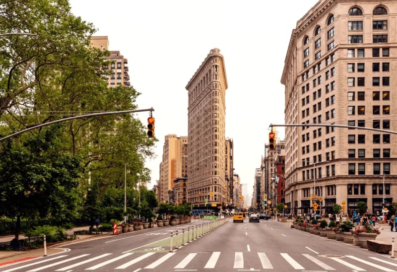 Split view of Madison Square Park with the Flatiron Building on one side and the NoMad hotel district on the other