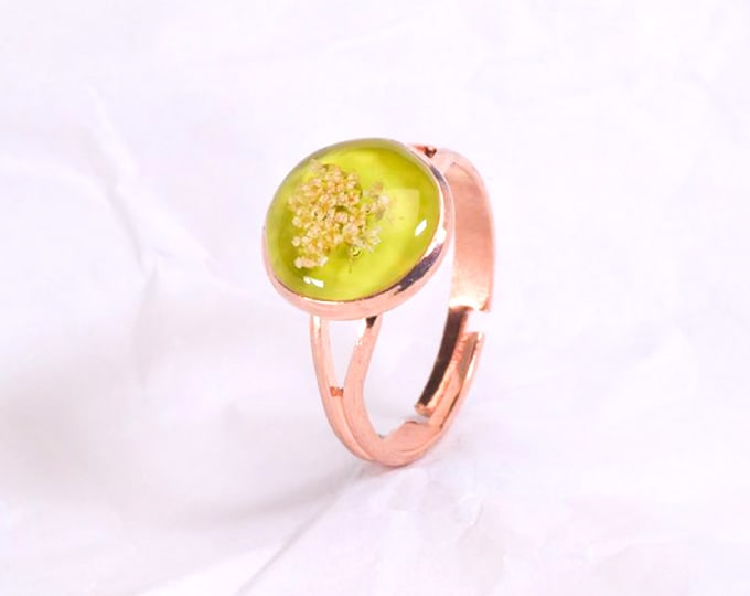 Rose gold metal ring with real flowers in resin on a green base