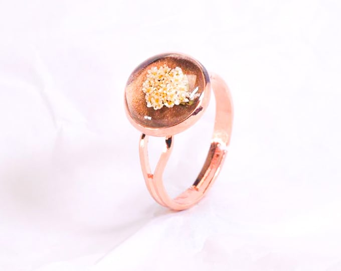 Anel de metal rosa ouro com base marrom e flores brancas em resina