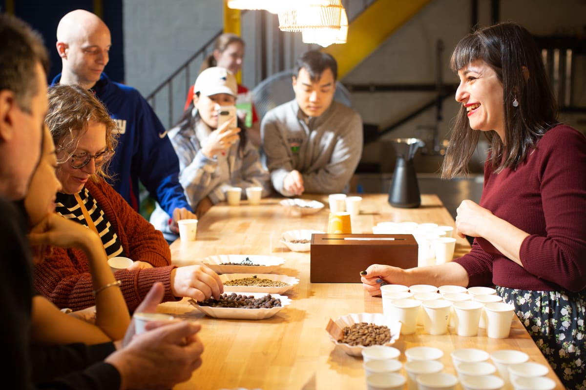 A smiling woman demonstrates the qualities of coffee bean roasting to a table of interested guests.