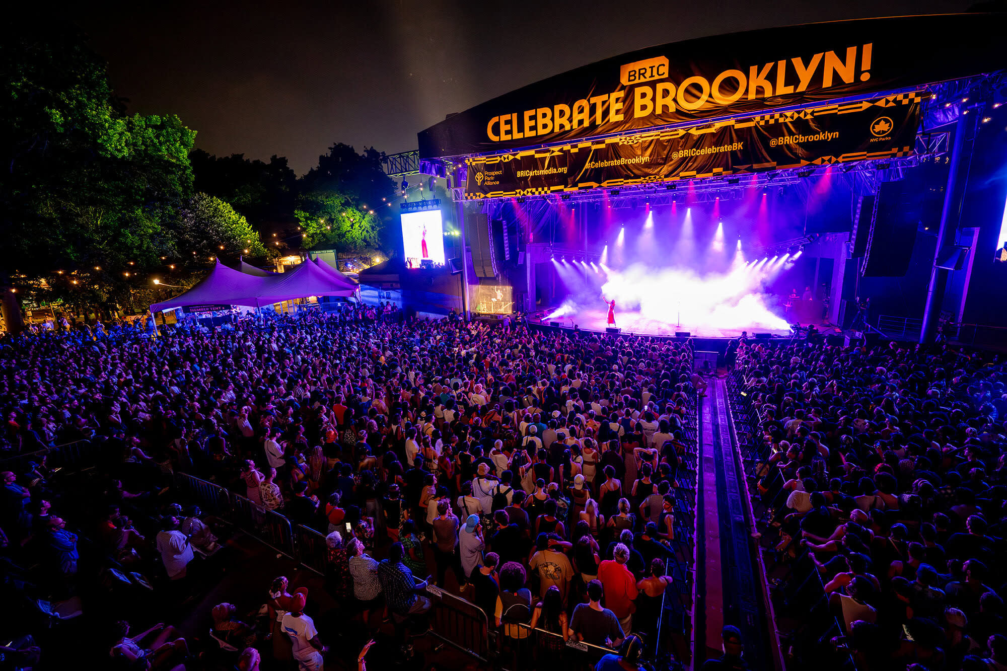 A large crowd watching a performance on a dramatically lit stage outdoors.