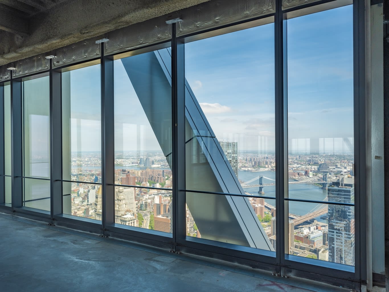 View of a city skyline and river through floor-to-ceiling windows in a modern high-rise building under construction.