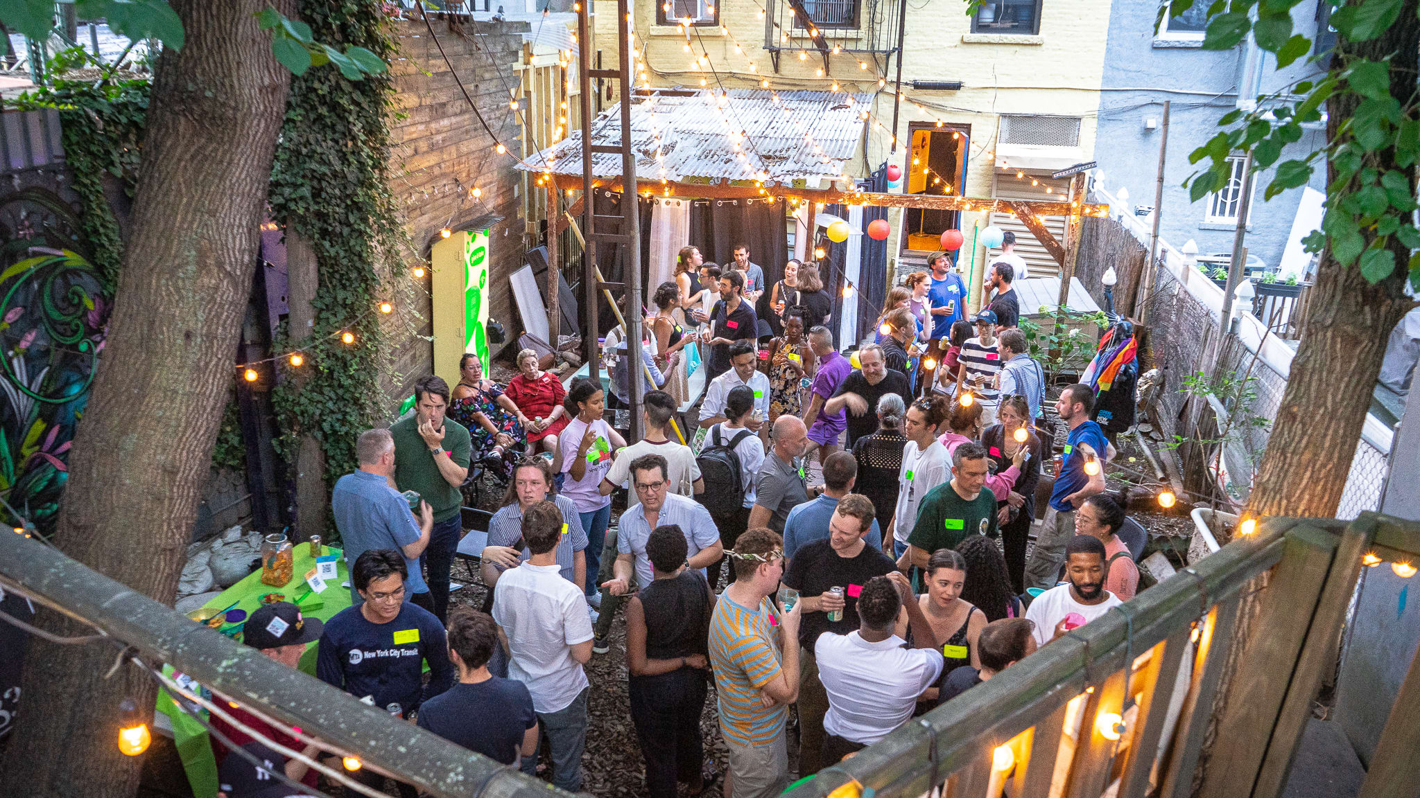 A lively outdoor party with many people socializing under string lights in a backyard setting.