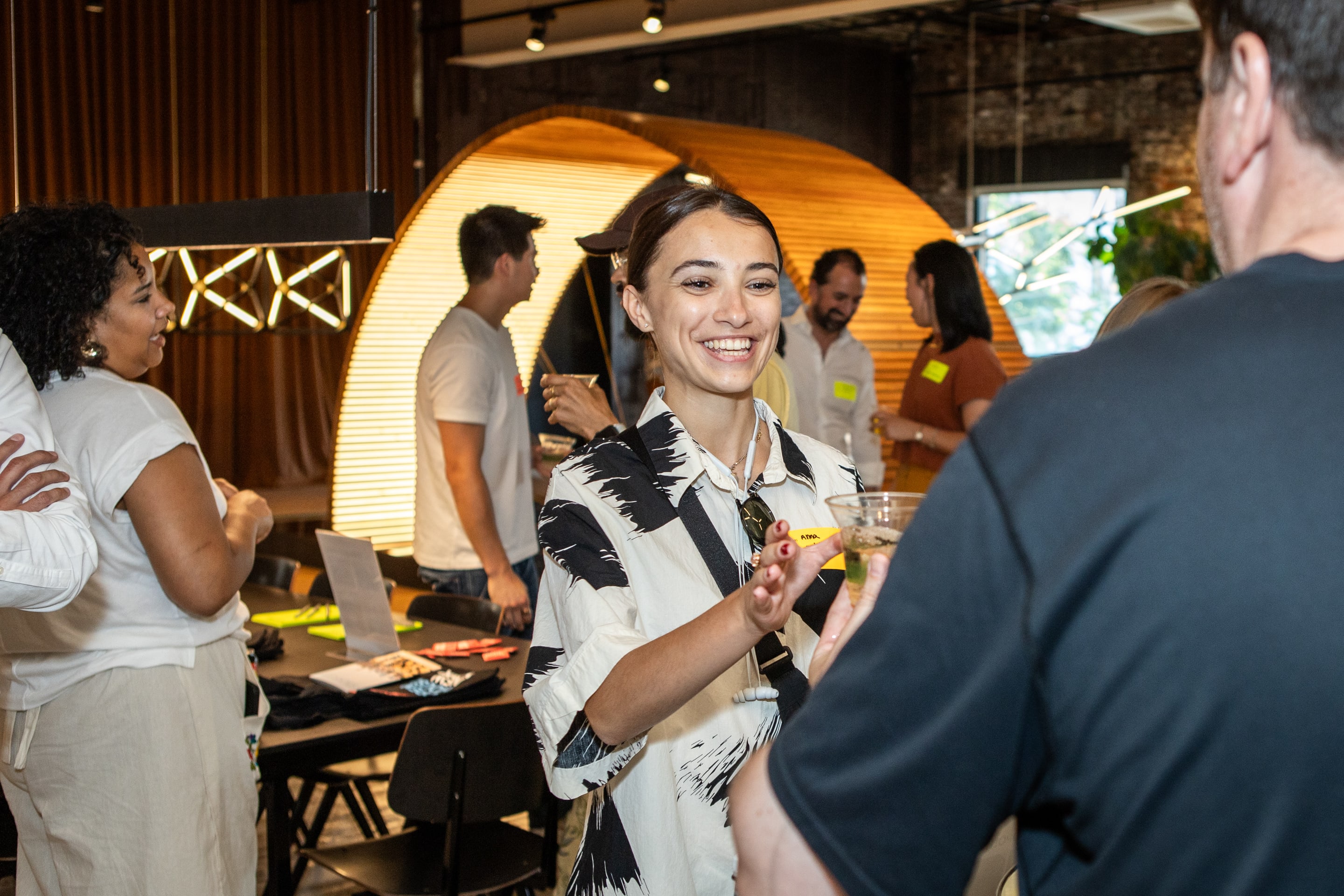 A woman smiling and talking with a man at a lively indoor social gathering or networking event.