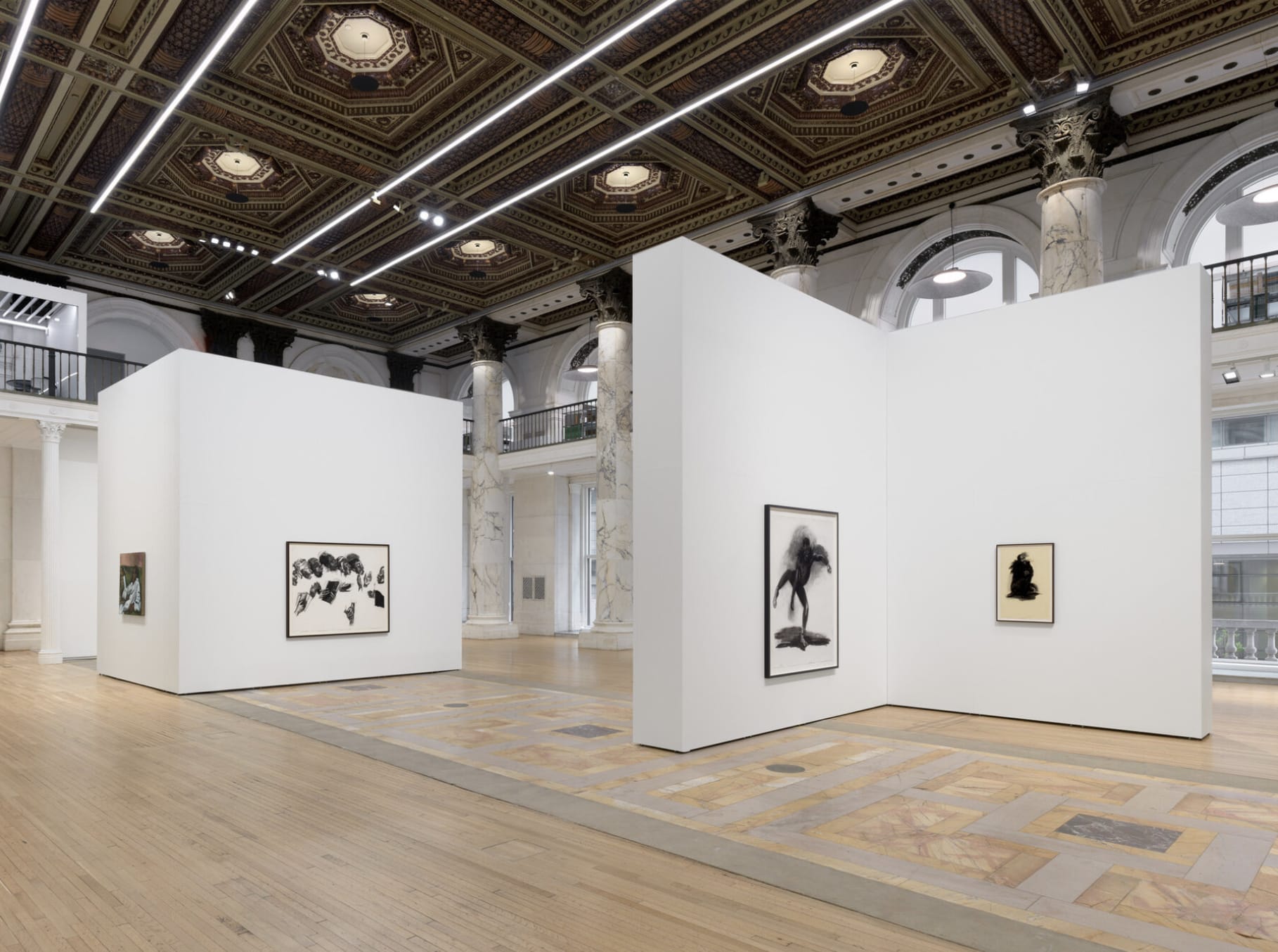 Grand hall with ornate coffered ceiling, in which freestanding walls display paintings of figures and abstract black and white images.