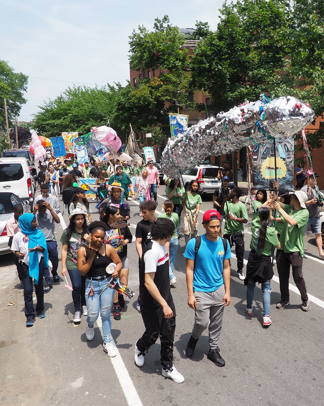 Marchers carry the signature eel puppet, made of shiny silver material and carried by six people on sticks overhead, in the 2023 Fish Parade. 