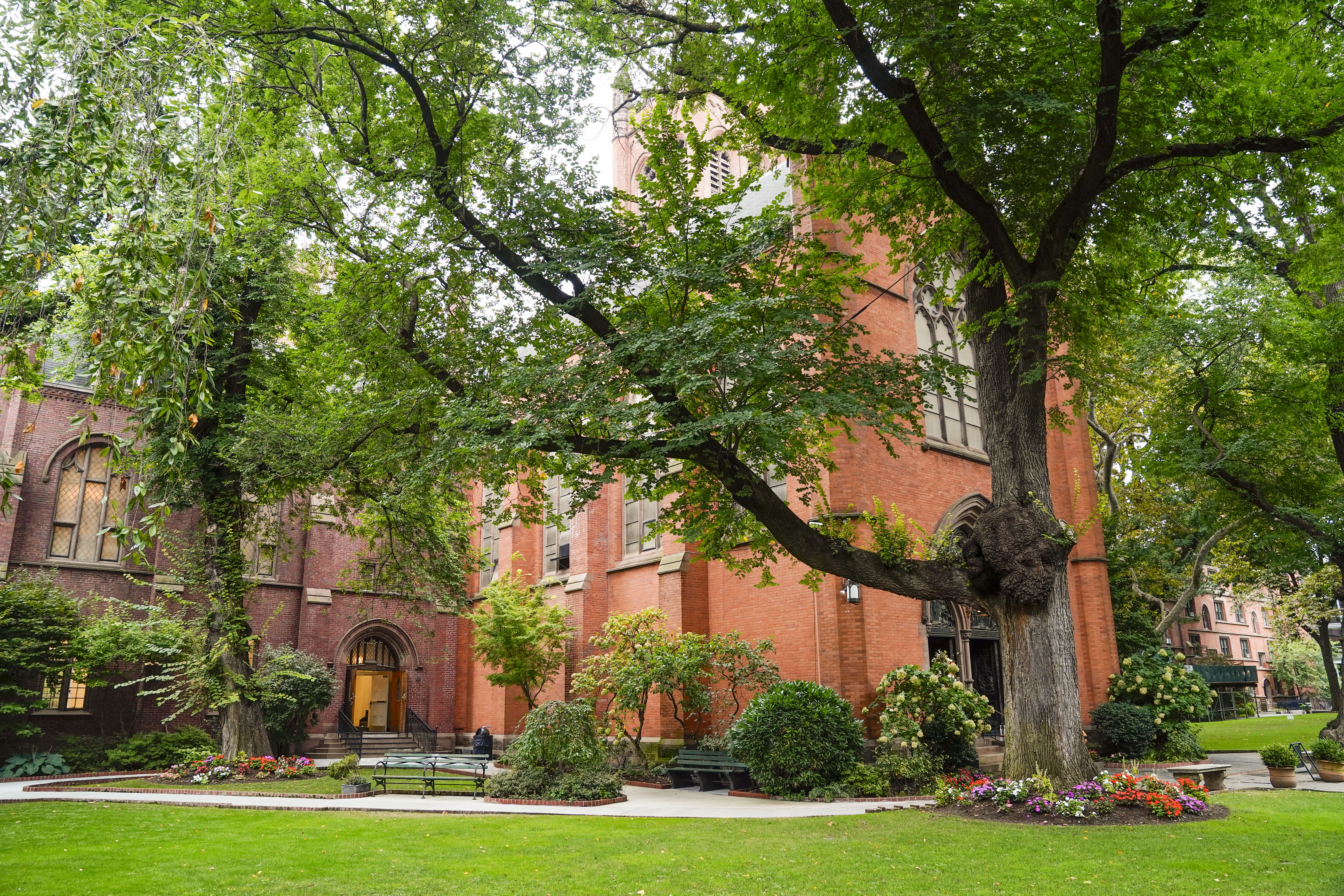 A large brick building with arched windows and a wooden door, surrounded by trees and green lawns.