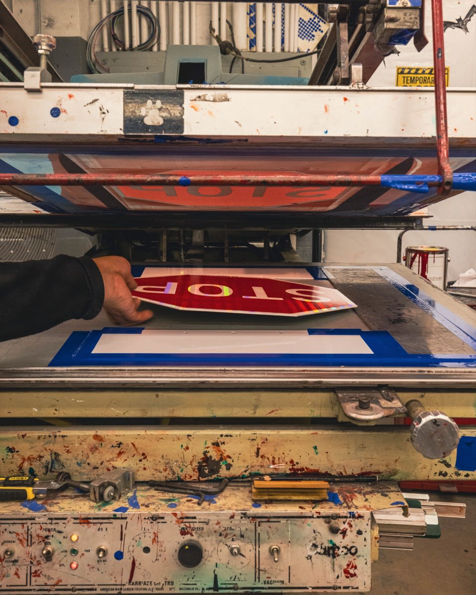 A person removes a freshly printed stop sign from a screen printing machine in a workshop.