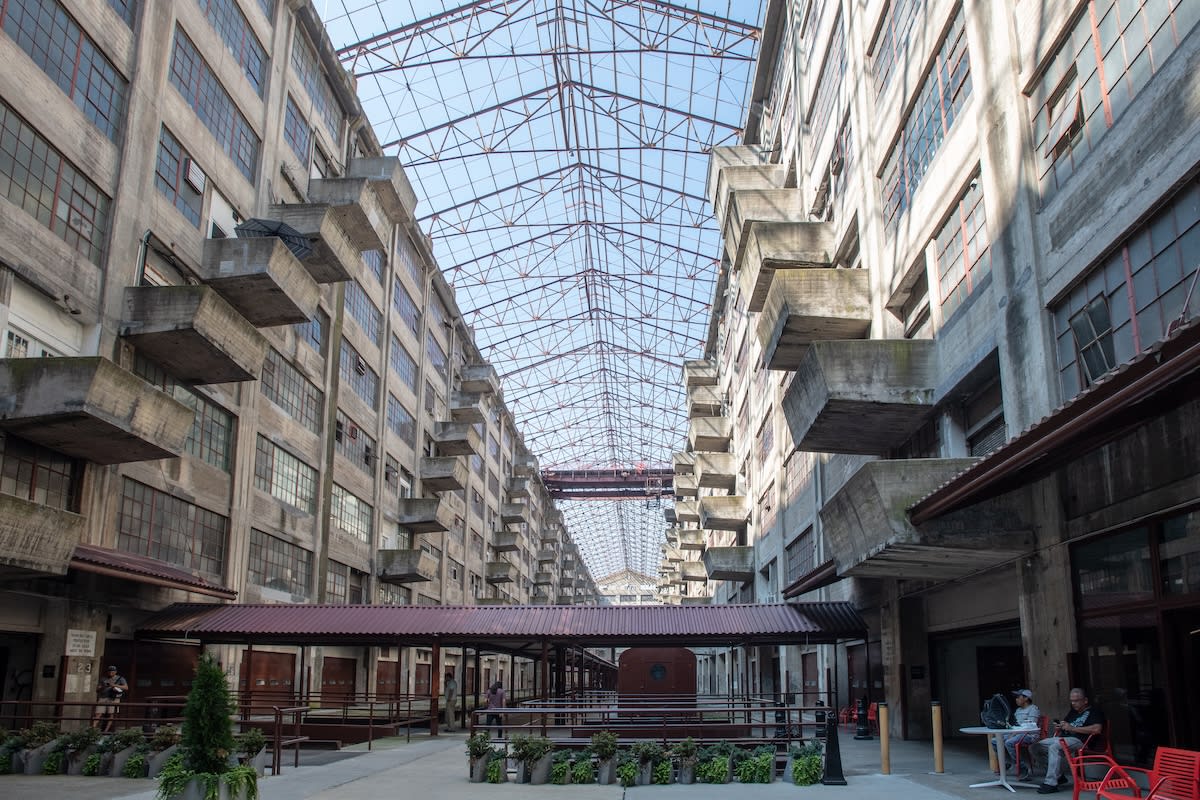 Industrial building interior with open walkways, balconies, glass roof, and outdoor seating on the ground level.