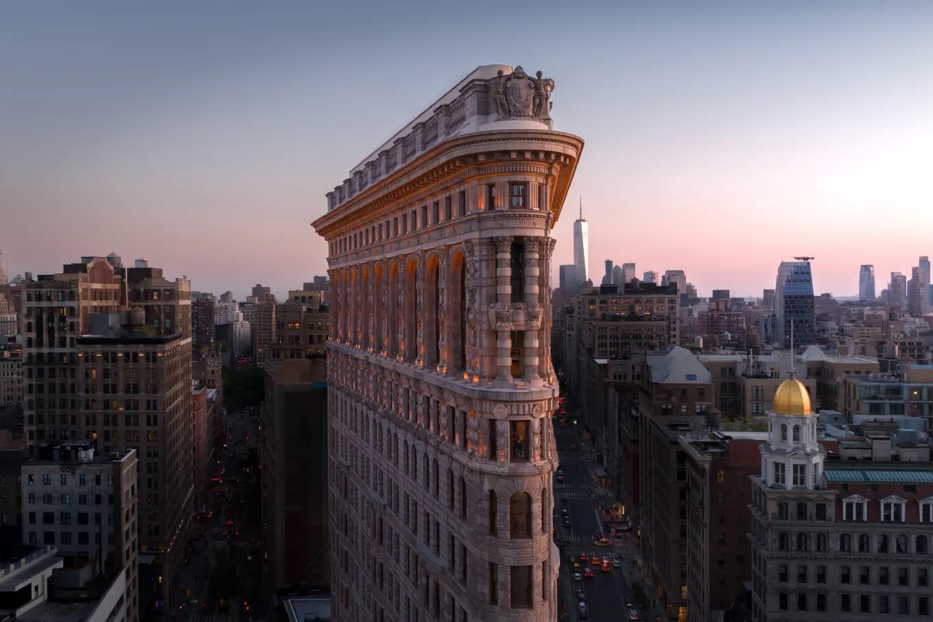 Flatiron Building at sunset, surrounded by city buildings, with the sky fading from blue to pink.