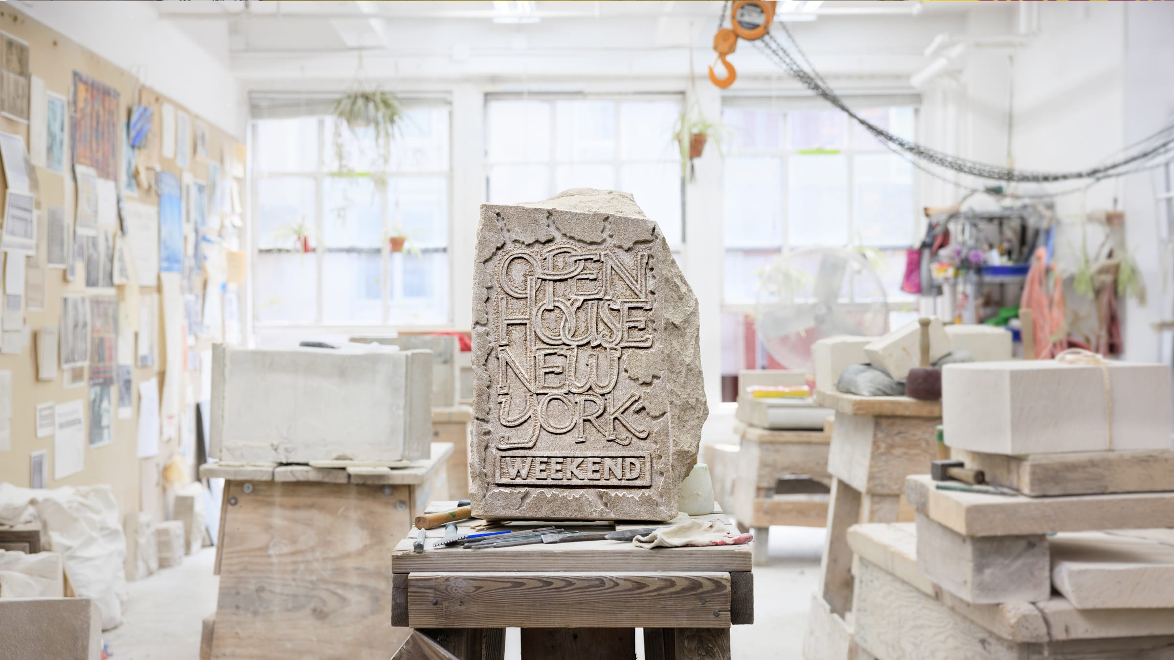 A stone sculpture engraved with Open House New York Weekend in a bright, busy studio workspace.