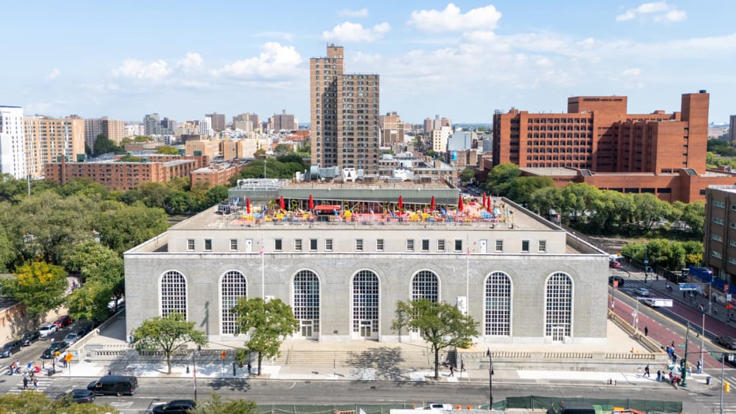 A large, gray building with arched windows and a colorful rooftop playground, surrounded by city buildings.