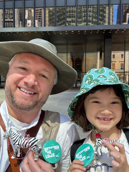 A parent and child pose with zebra toys. They are wearing safari hats and smiling.