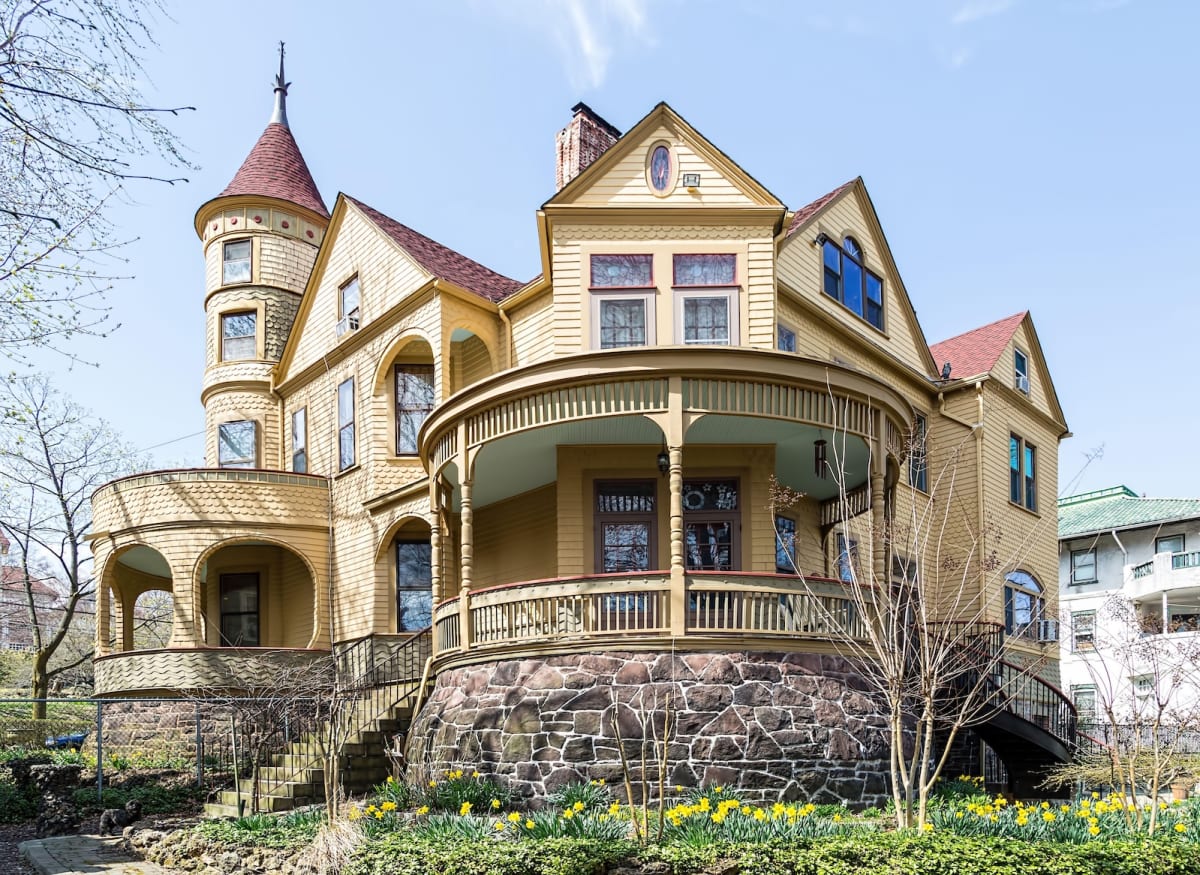 Large yellow Victorian style house with a turret, several gables, and two large circular porches.