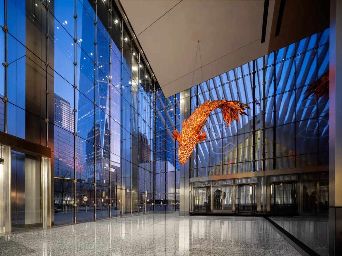 A large copper sculpture of a fish, lit from within, is suspended in a glass-walled lobby. 