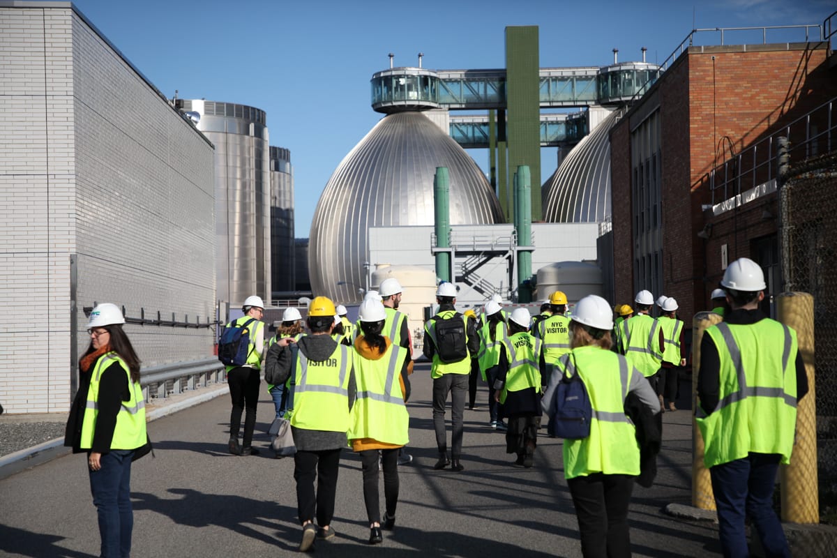 A group of people in safety gear tour an industrial facility with large dome-shaped structures.