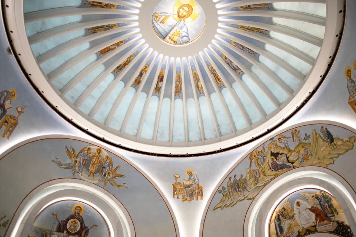 Domed church ceiling with religious iconography and frescoes of saints under radiating white ribs.