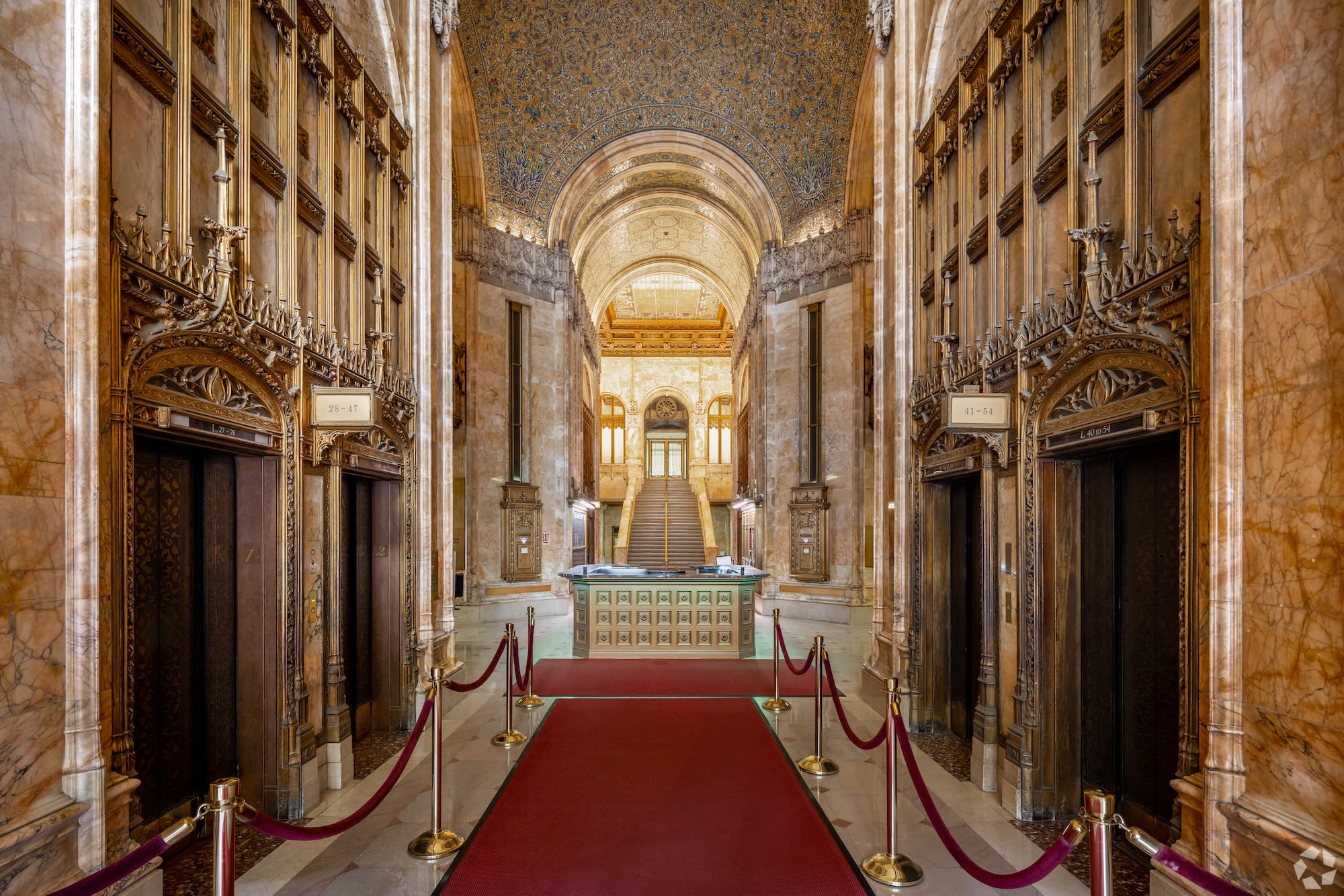 Ornate theater interior with red seats, golden decor, and a stage with a closed gold curtain under arch.