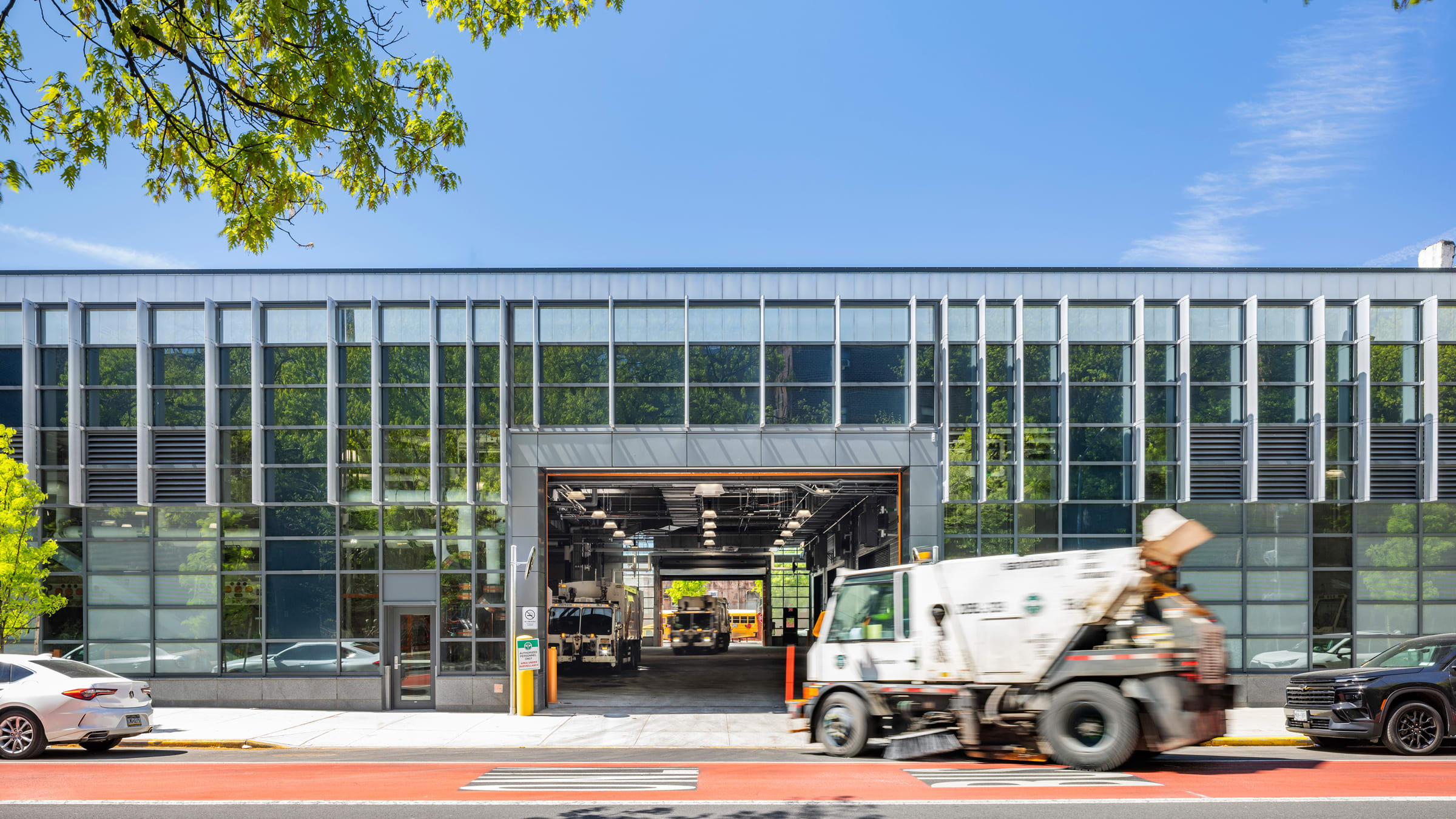 A truck exits a modern glass-paneled building on a sunny day.