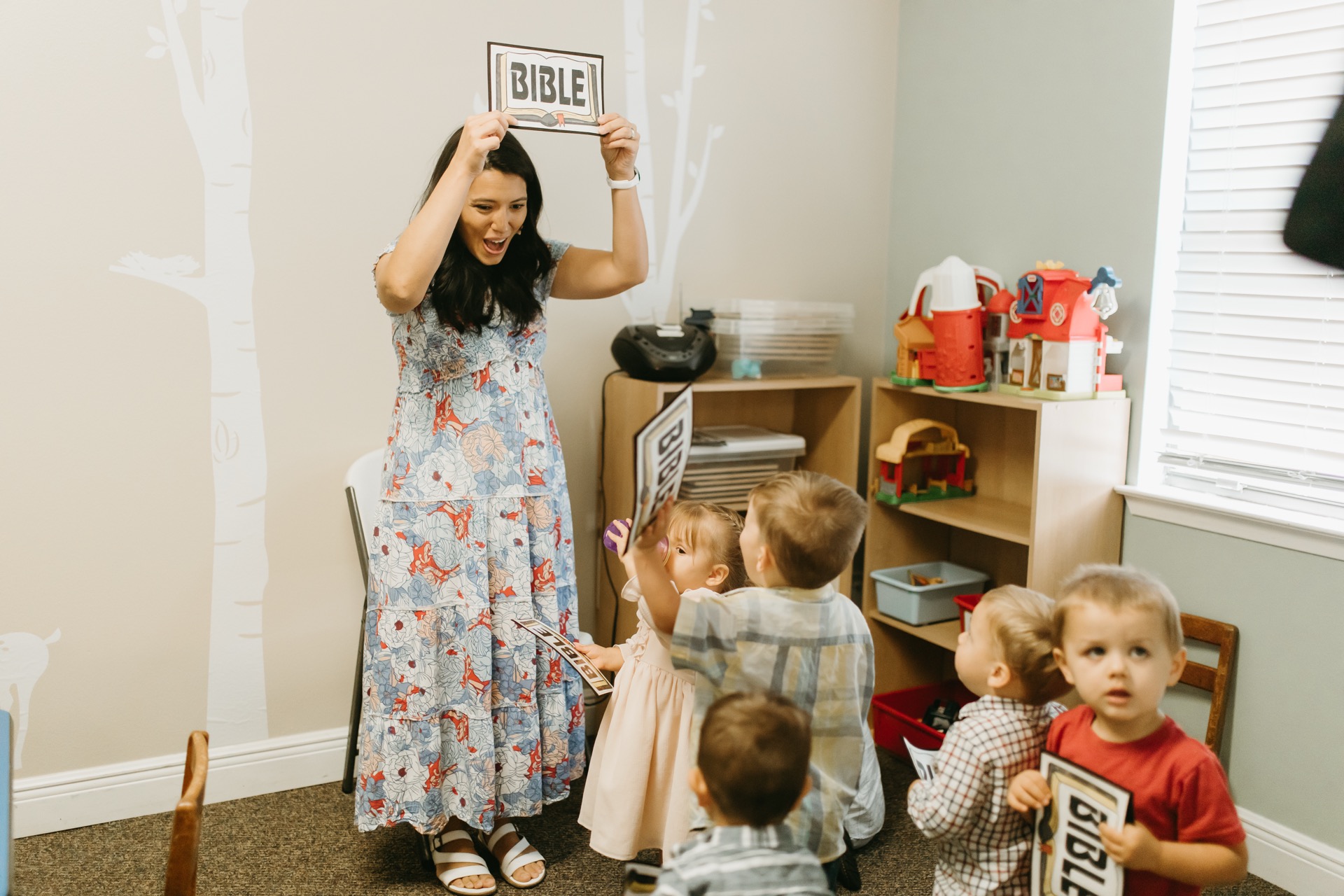 Teacher holding BIBLE sign with toddlers