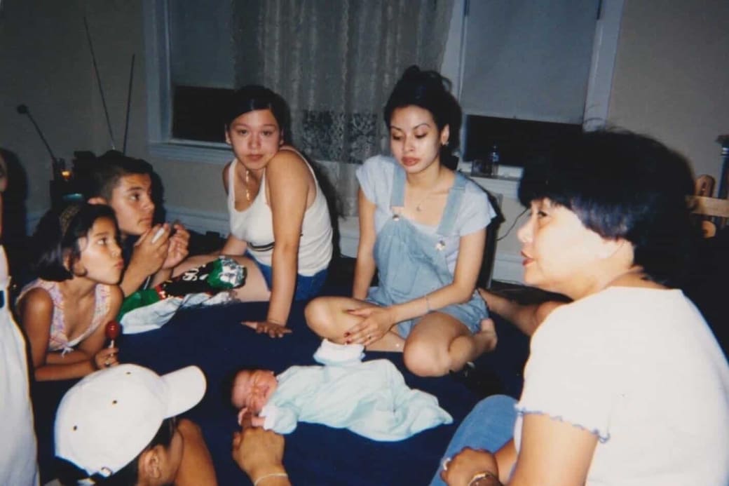 Group of adults and children sit in a circle around an infant lying down in a home