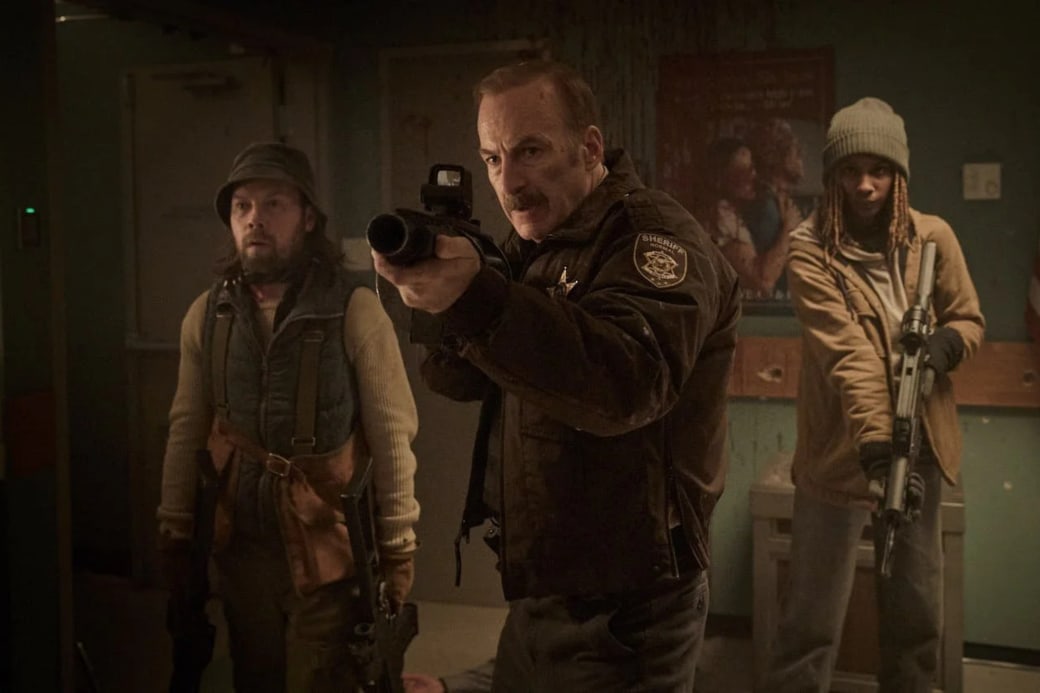 A sheriff holding a gun is flanked by two other people.