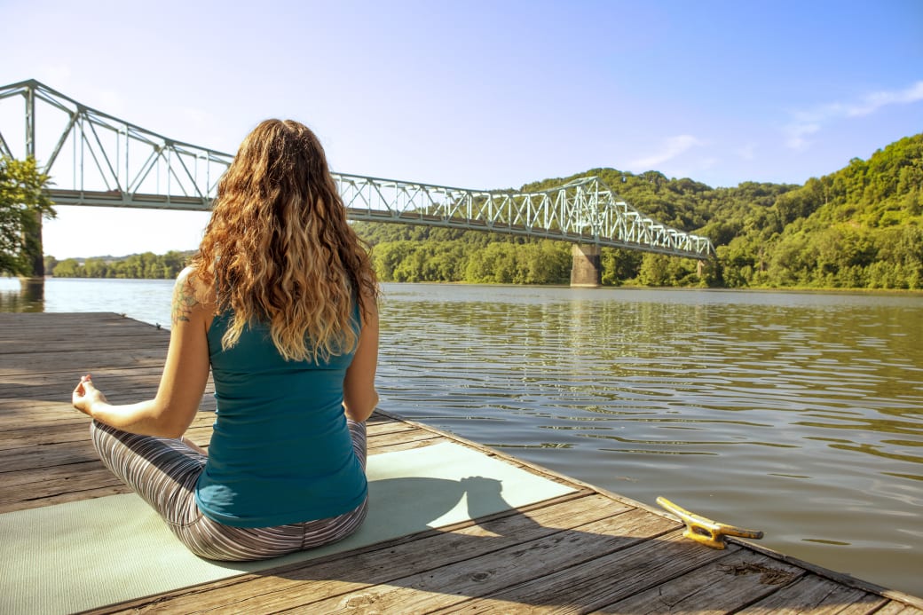 A person in a yoga pose in front of the Allegheny River.