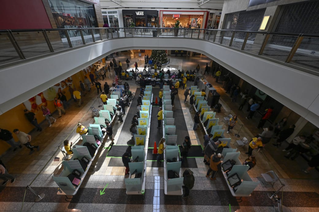 Poll workers in yellow shirts look over people voting in voting booths set up at a mall.